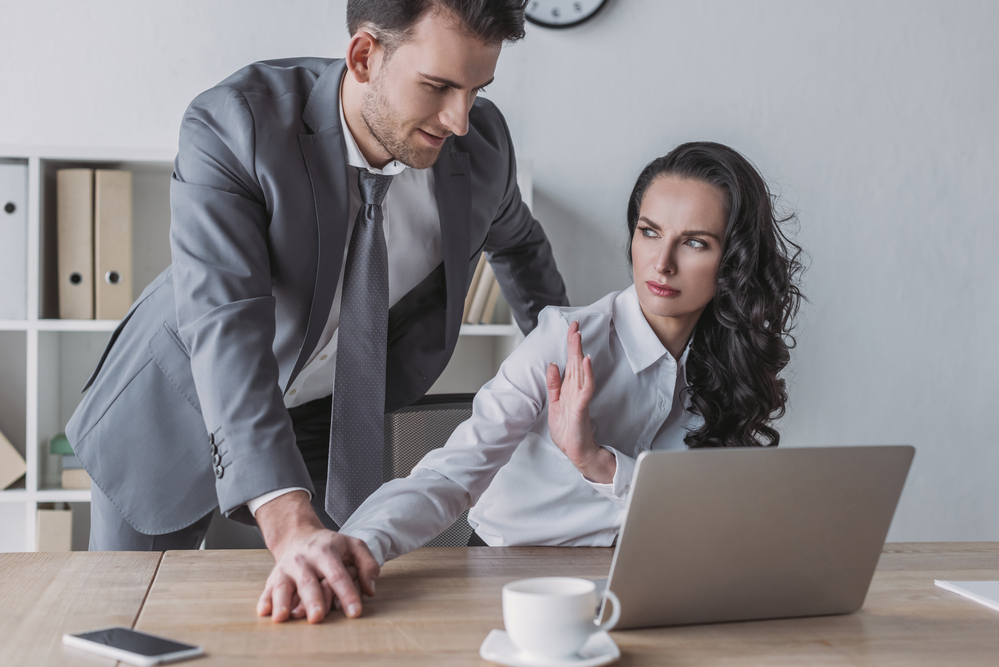 Male colleague placing an unwanted hand on a female colleague's shoulder, illustrating workplace harassment.