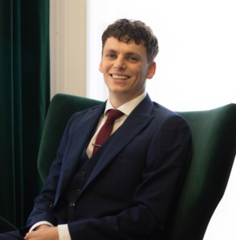 Alexander Ashcroft, founder and director of Locate Solicitors, seated in a professional setting wearing a navy suit and red tie, symbolising trust and professionalism.